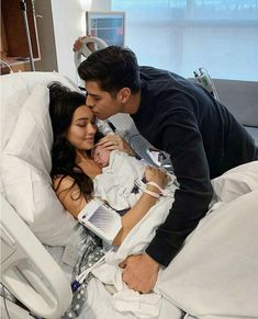 a man kissing a woman on the cheek in a hospital bed while holding a baby