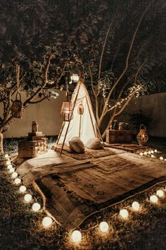 a teepee is lit up in the dark with candles around it and lights on the ground