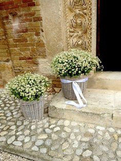 two baskets filled with flowers sitting on the side of a stone walkway next to a doorway