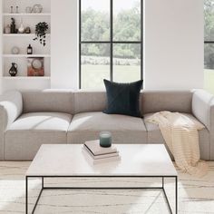 a living room with a couch, coffee table and books on the floor in front of large windows