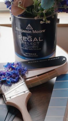 a paint can and brush sitting on top of a table next to some blue flowers