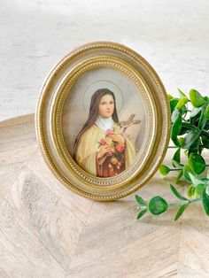 an image of the virgin mary holding flowers in a gold frame on a wooden table