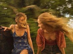 two young women sitting on the back of a boat in the water, one with her hair blowing in the wind