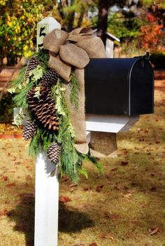 a mailbox decorated with pine cones, evergreens and burlap bow tied to it