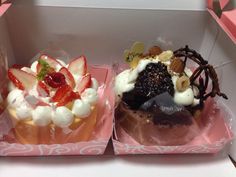 two cupcakes with strawberries and other toppings are in a pink box