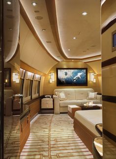 the inside of an airplane with couches, tables and television on the wall above