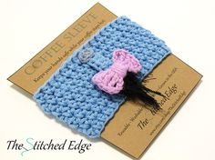 a blue and pink crocheted hair clip with a black feather on it's end