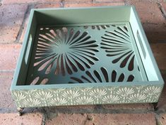 a green box sitting on top of a red brick floor next to a planter