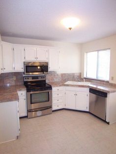 an empty kitchen with white cabinets and stainless steel appliances