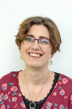 a woman with glasses smiling for the camera while wearing a red shirt and black top