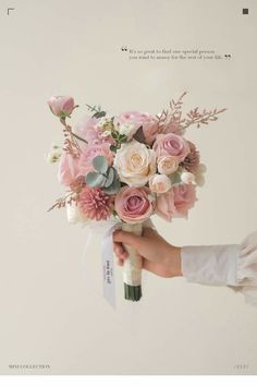 a person holding a bouquet of pink and white flowers with a quote on the wall in the background