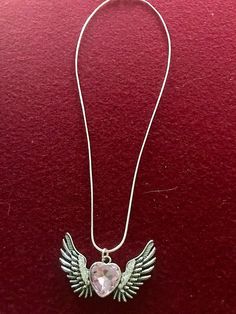 an angel wing necklace with a heart shaped crystal in the center on a red background