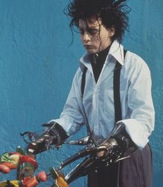 a man in white shirt and black suspenders holding two pairs of gloves on his hands