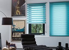 a living room filled with black furniture and lots of windows covered in blue blind shades