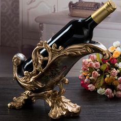 a wine bottle holder on a table next to flowers and a vase with roses in it