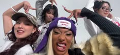 four women wearing hats and fur coats posing for the camera with their hands in the air