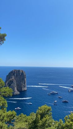 boats are in the water near some rocks and trees on a clear blue sky day