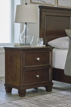 a night stand with two glasses on it next to a lamp and bed in a bedroom