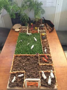 a wooden table topped with lots of dirt and grass covered in small animals on top of it