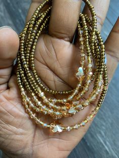 a hand holding three strands of gold colored beaded necklaces with clear crystal beads