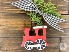 a red train ornament hanging on a wooden wall next to a pine tree