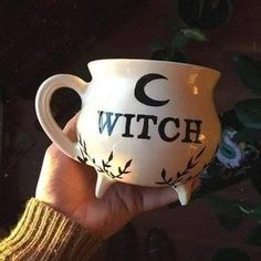 a hand holding a white mug with the word witch painted on it's side