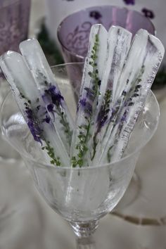 there are some ice sticks in the glass cup on the table with purple and white flowers