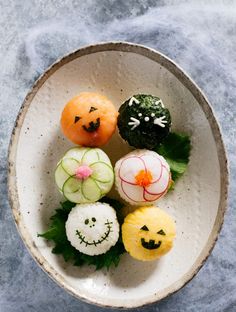 a white bowl filled with different types of sushi on top of a blue surface