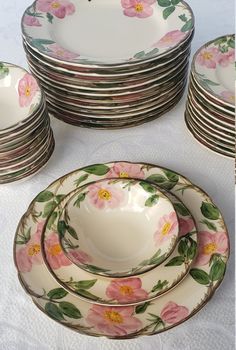 a table topped with lots of plates covered in pink and green flowers on top of white cloth