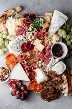 an assortment of cheeses and meats on a platter with grapes, nuts