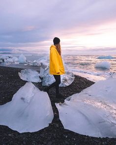 a woman in yellow jacket standing on beach next to icebergs