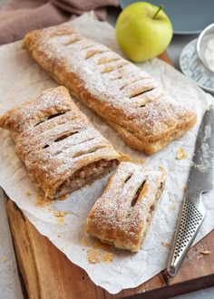 two pastries sitting on top of a cutting board next to an apple and knife