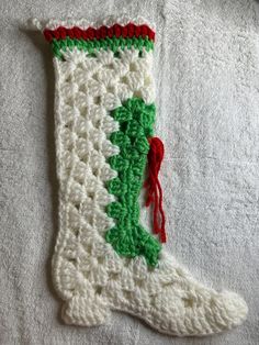 a crocheted christmas stocking hanging on a white towel with red and green trim