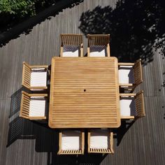 an overhead view of a wooden table and chairs on a deck with trees in the background