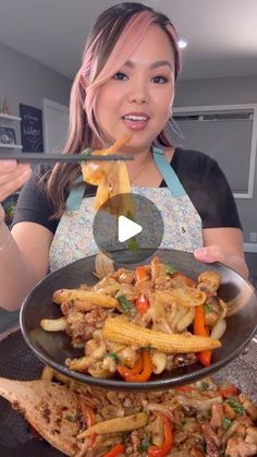 a woman holding a pan full of food with chopsticks in her hand and an image of chicken, corn on the cob