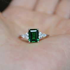 a woman's hand holding an emerald and diamond ring