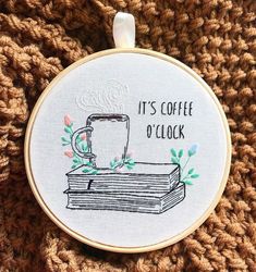 a cross stitch ornament that says it's coffee o'clock on top of a stack of books