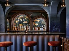 three stools in front of a bar with stained glass windows and fish paintings on the wall