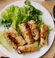 a white plate topped with meat and lettuce next to a bowl of sauce