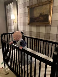 a baby sitting in a crib looking at something on the ground next to him