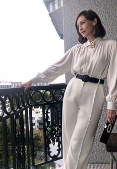 a woman is standing on a balcony with her hand in her pocket and looking off to the side