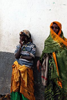 two women standing next to each other near a wall with their heads covered in scarves