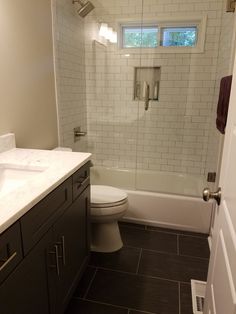 a white toilet sitting in a bathroom next to a sink and bathtub under a window