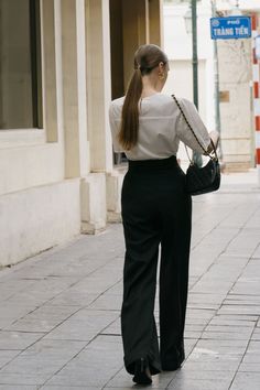 a woman walking down the street with her back turned to the camera and holding a purse