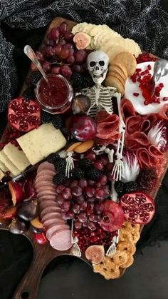 a wooden platter filled with cheese, crackers, fruit and skeleton figurines