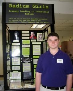 a young man standing in front of a display case with papers on it and information about raddum girls