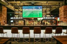 a bar with several chairs and a large screen on the wall behind it in a sports stadium