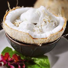 a plate topped with a bowl filled with coconut and whipped cream on top of leafy greens