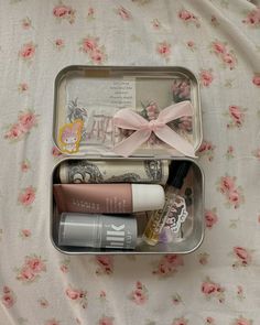 an open tin with various items in it sitting on a floral print bed sheet,