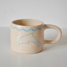 a coffee cup with a dolphin drawn on it's side sitting on a table